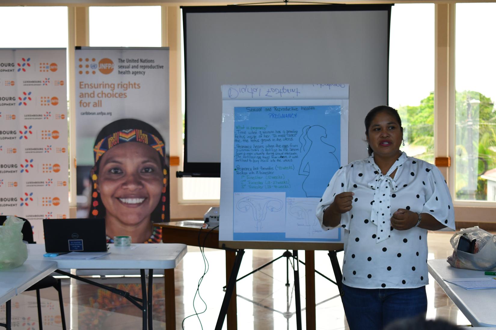 Woman standing next to a flip chart and banner, delivering a lecture