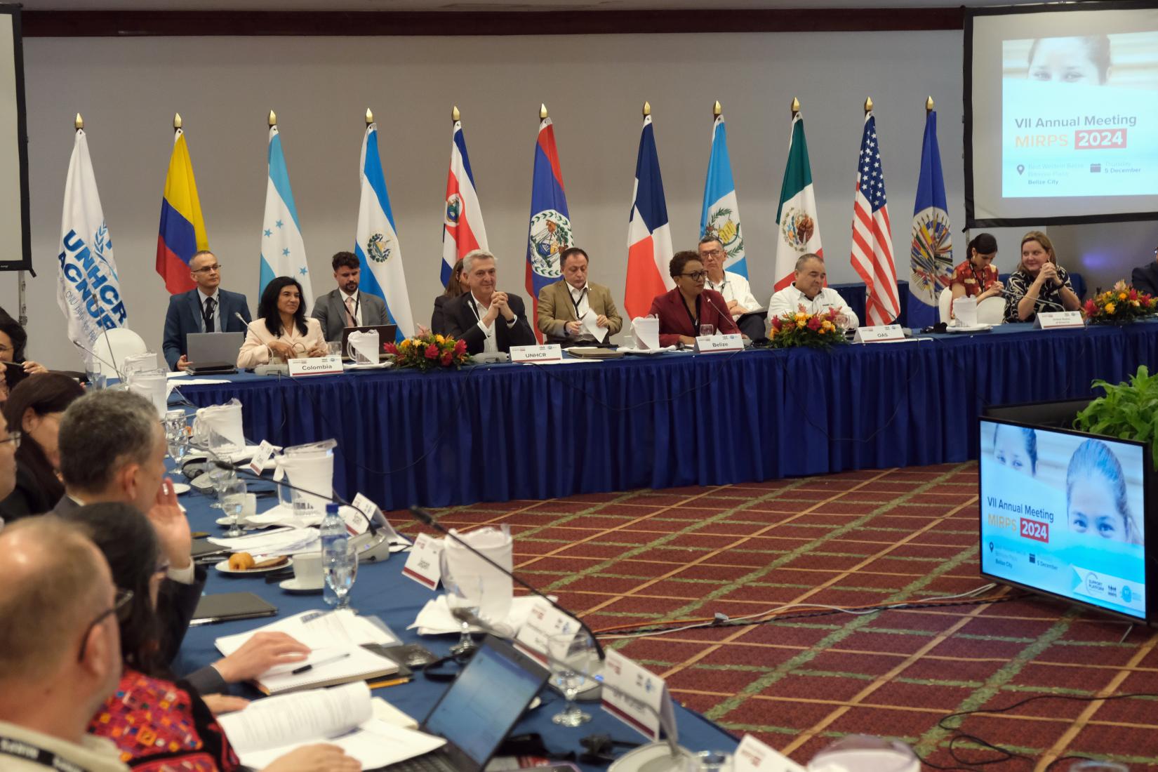 Meeting participants seated along two sides of a hollow rectangular table.