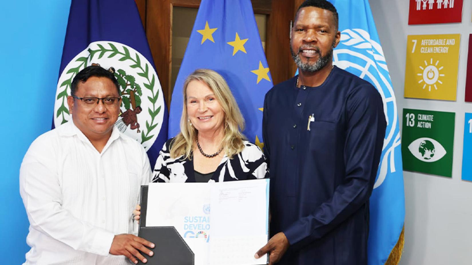 Three individuals - one woman flanked by two men - stand before flags and SDG icons at on the right